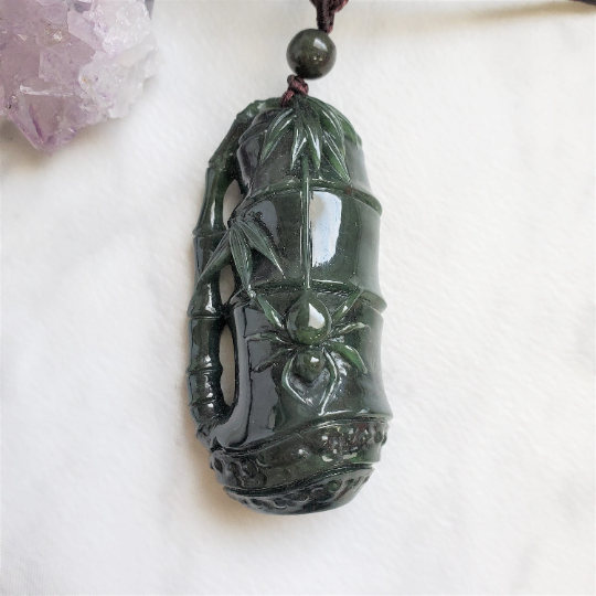 Dark green jade spider pendant on a brown cord with a round bead against a light background.