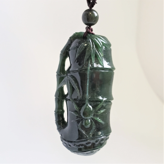 Dark green jade pendant carved as a bamboo stalk with a spider motif, suspended from a cord with a bead.