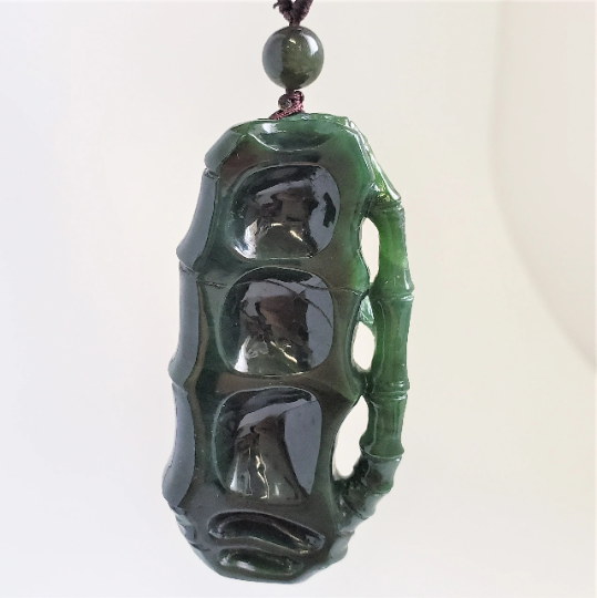 Green jade spider pendant suspended by a brown cord against a white background.
