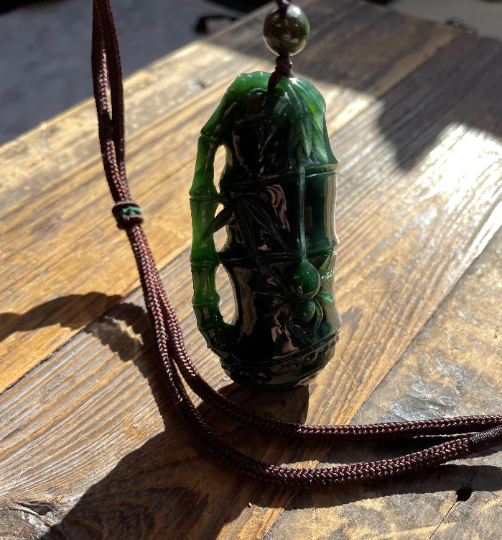 Side view of a green jade spider pendant on a wooden surface, attached to a brown cord with a bead.