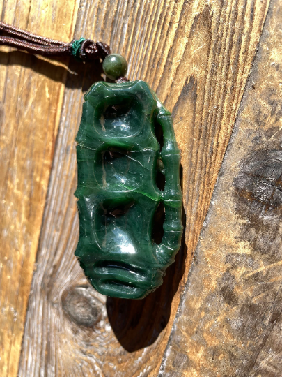 Close up of green jade spider pendant showing intricate carved body with open spaces suspended from brown cord