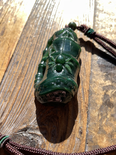 Dark green jade spider pendant carved with segmented body resting on a wooden surface with a brown cord.