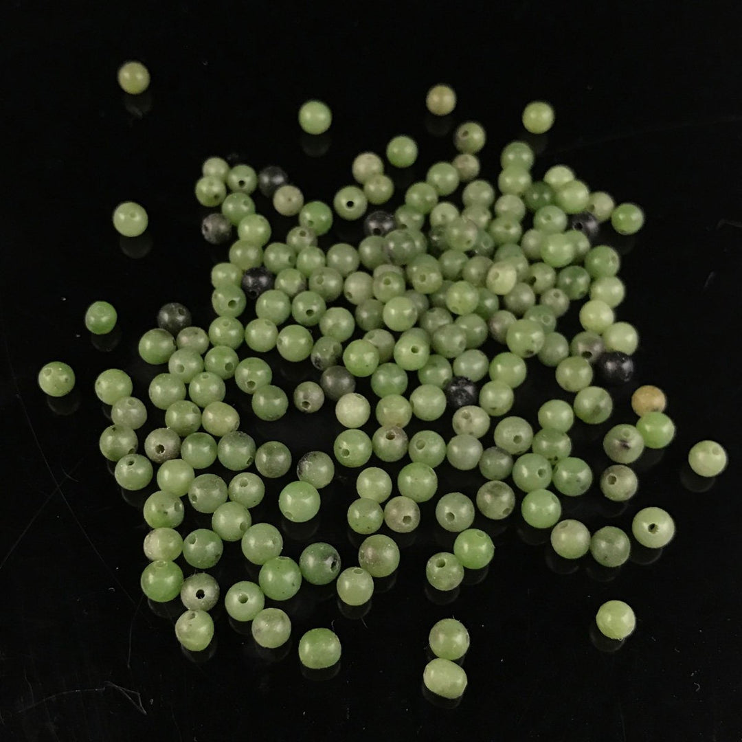 Assorted 3-4 mm Canadian Jade beads scattered on a black background