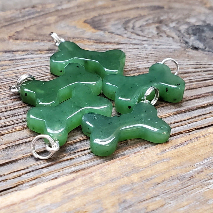 Green bone shaped charms with silver loops laid on a wooden surface