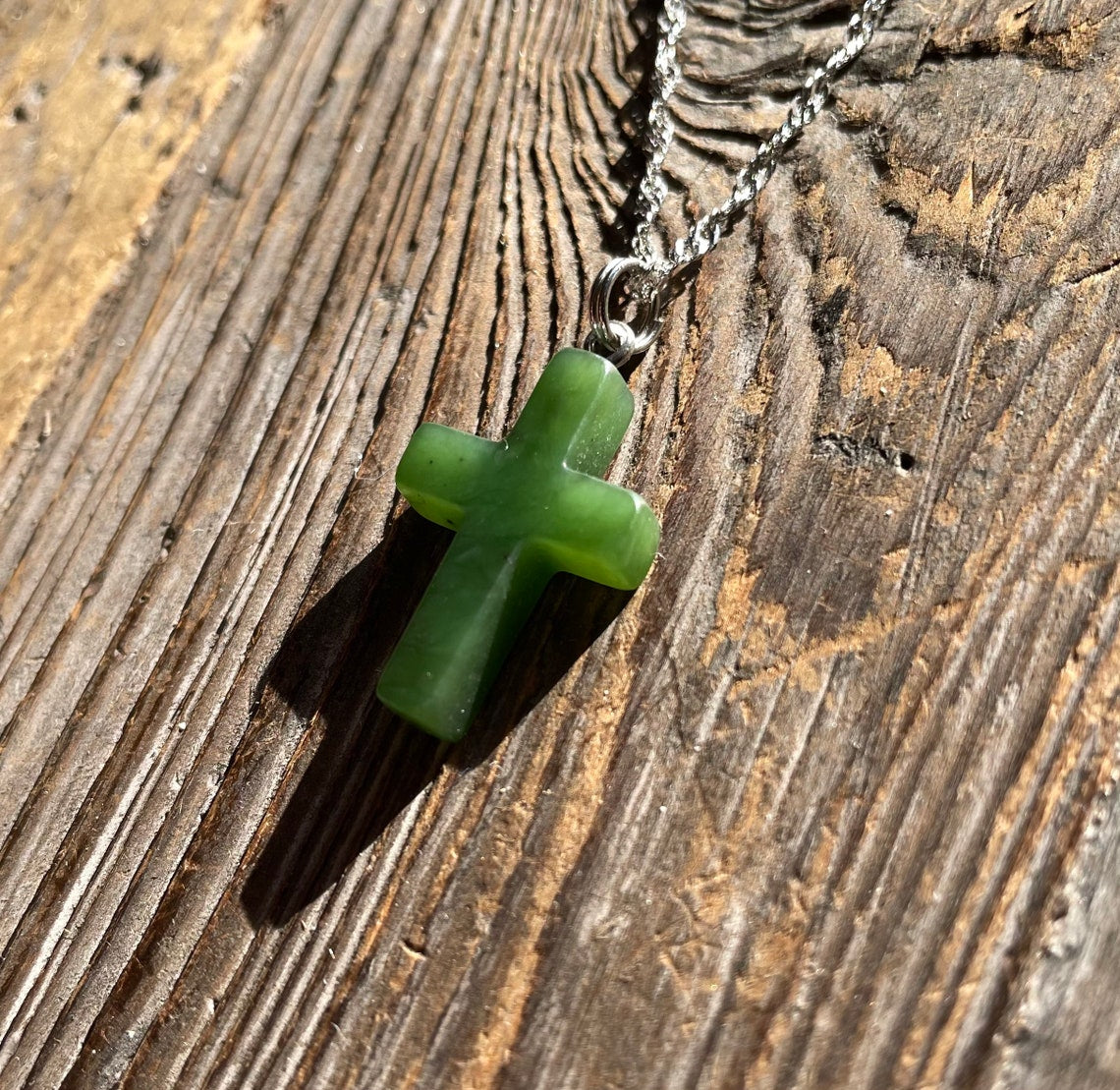 Small jade cross pendant on a silver chain resting on wood