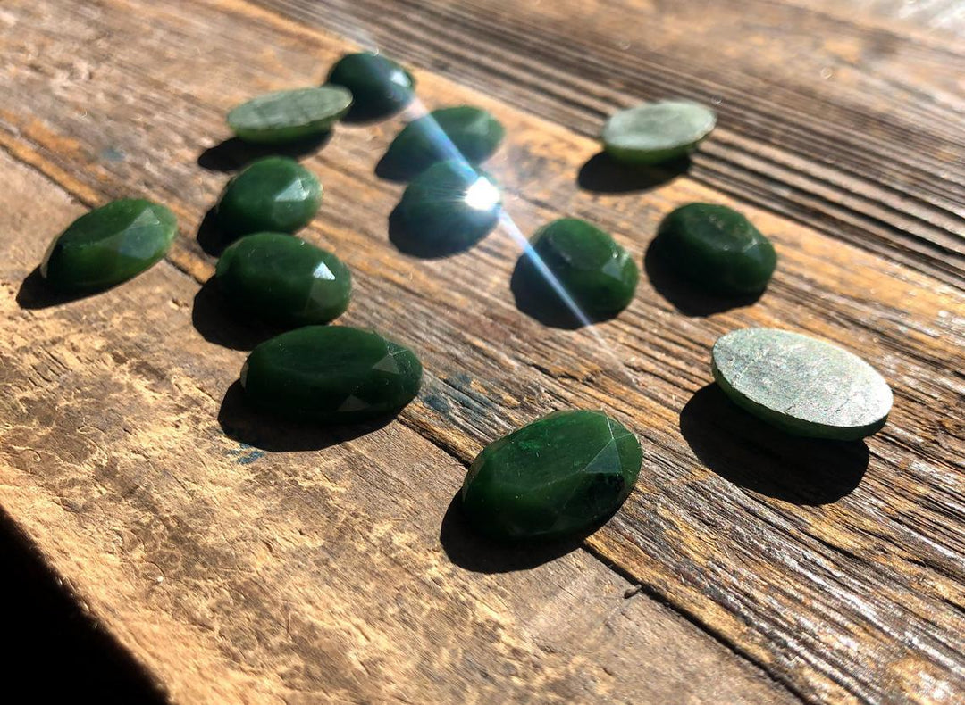 Dark green faceted oval cabochons 13x18mm shown from above on wood