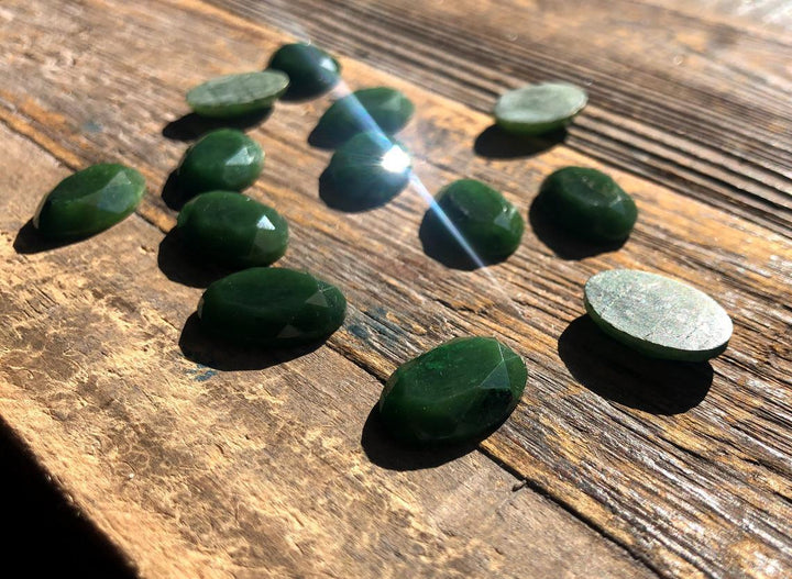 Dark green faceted oval cabochons 13x18mm shown from above on wood