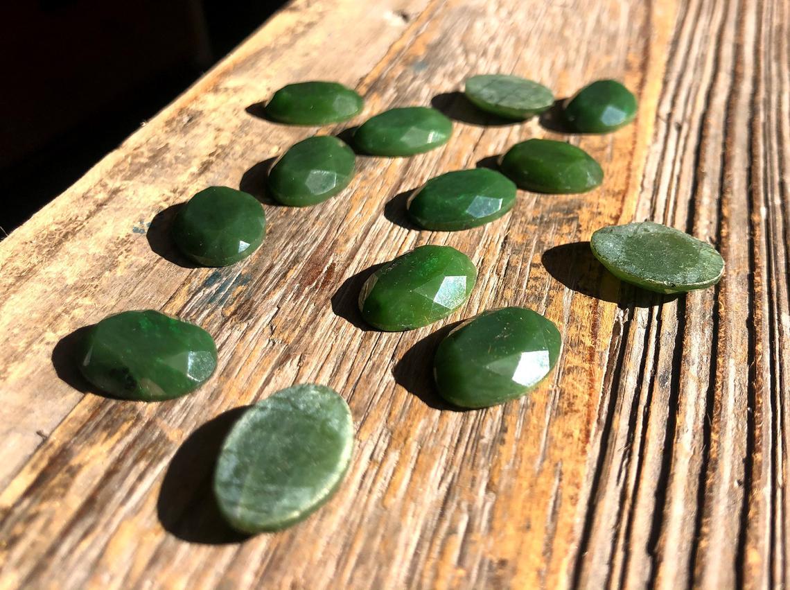 Dark green faceted oval cabochons 13x18mm scattered on a wooden plank