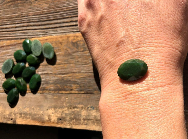 Single dark green 13x18 mm faceted oval cabochon on a forearm for size reference.