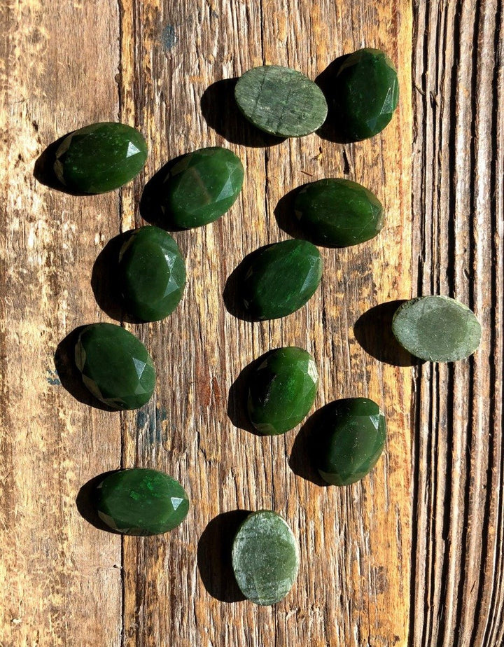 Dark green 13x18 mm faceted oval cabochons scattered on weathered wood.