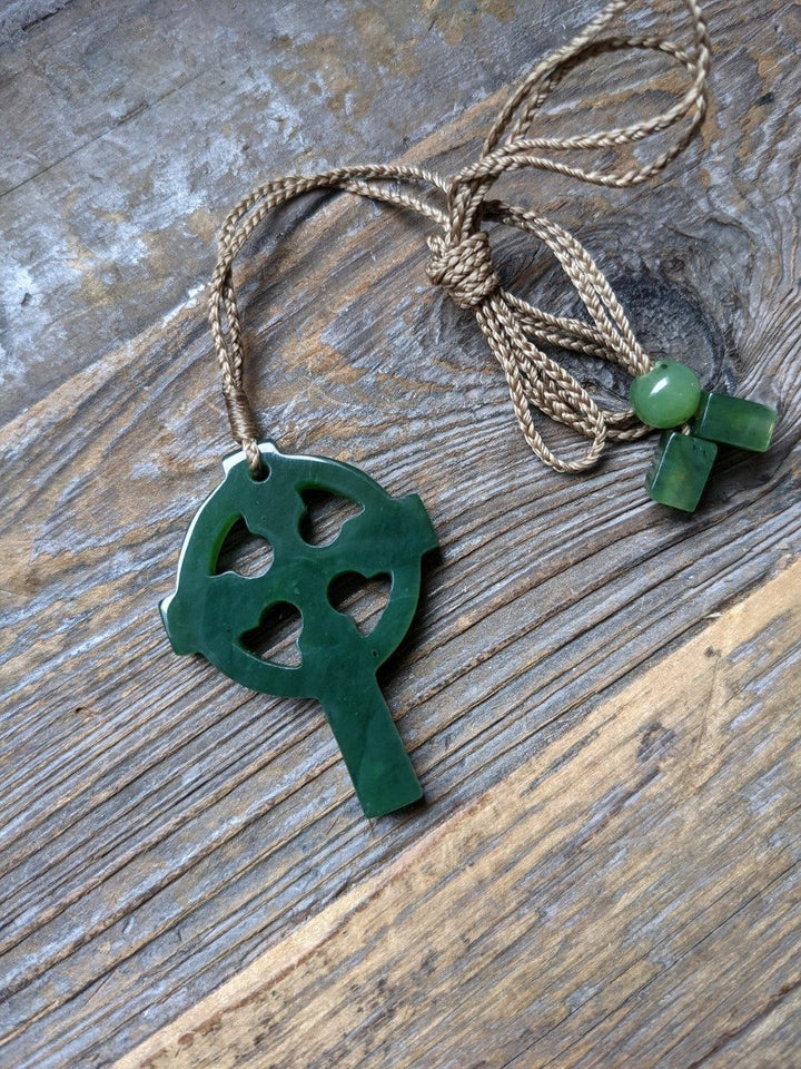 Green jade cross pendant on a braided brown cord with small green beads