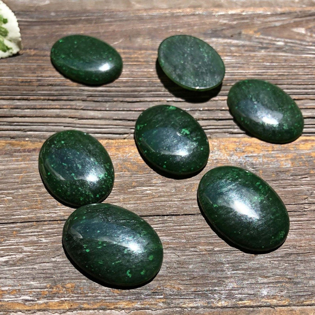 Dark green oval Cassiar jade cabochons arranged on a weathered wooden surface