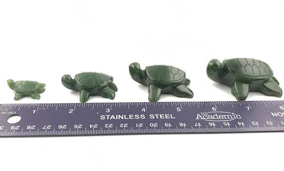 Four green turtle figurines arranged in a row with a measuring ruler for scale