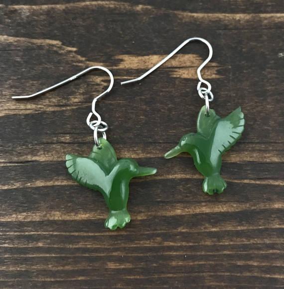 Green hummingbird shaped earrings with silver hooks on a wooden background