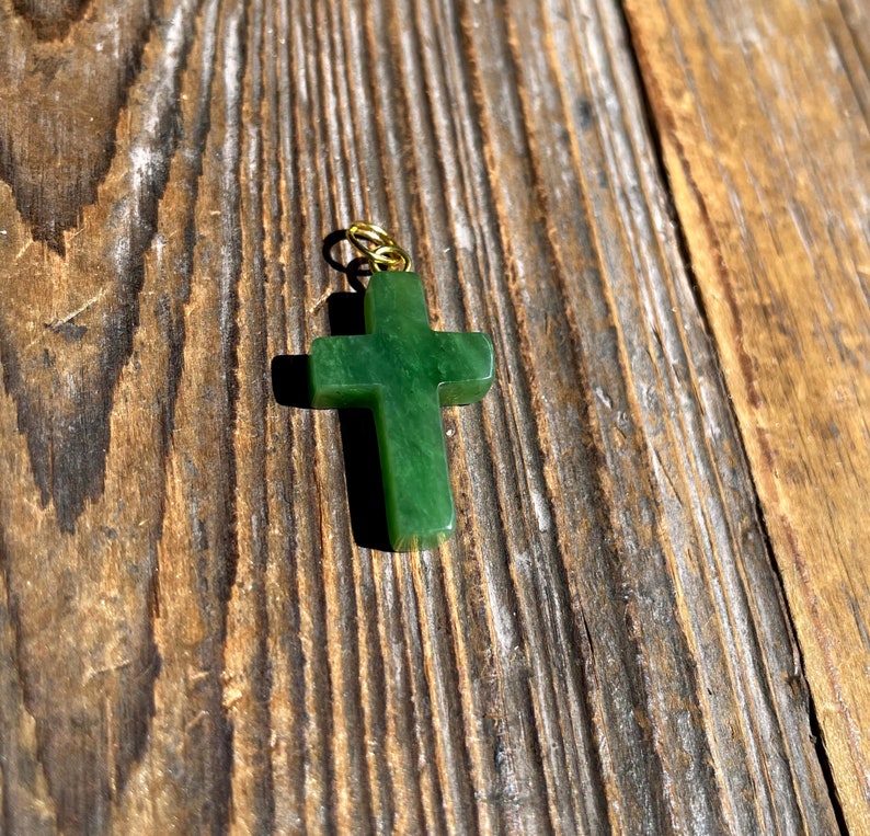 Close up of jade cross pendant on a rustic wood surface with chain