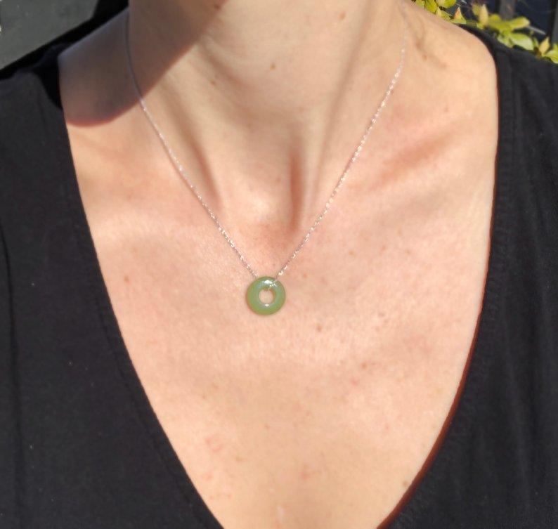 Green jade donut pendant on a silver chain worn as a necklace