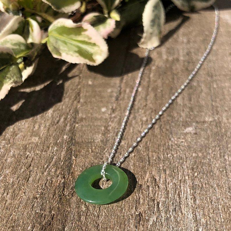 Green jade donut pendant 15mm on a silver chain resting on a wood surface.