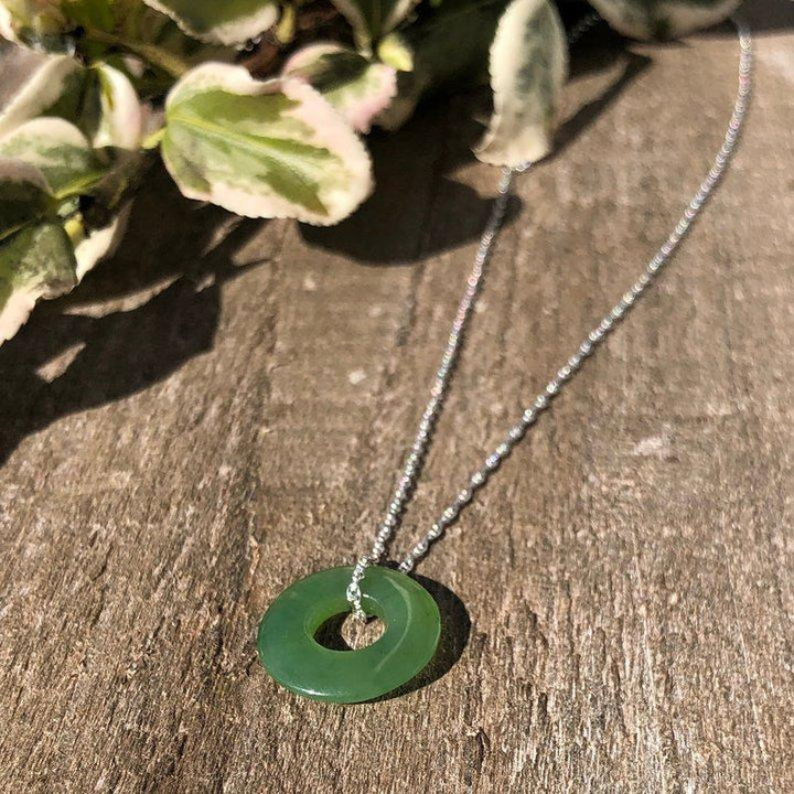 Green jade donut pendant 15mm on a silver chain resting on a wood surface.