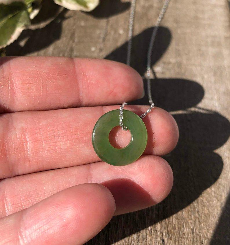 Close up of green jade donut pendant held between fingers with a silver chain.