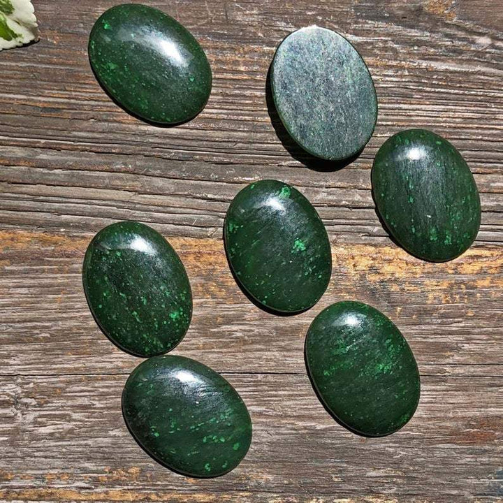 Dark green oval Cassiar jade cabochons arranged on a weathered wooden surface