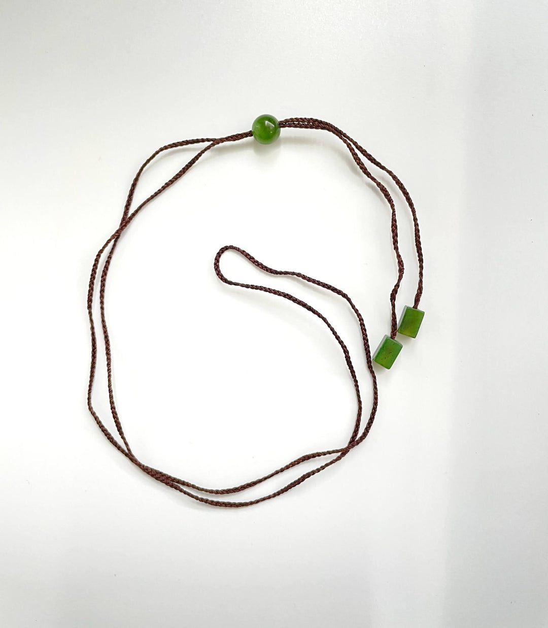 Brown braided cord necklace featuring a single round jade bead and two square jade beads
