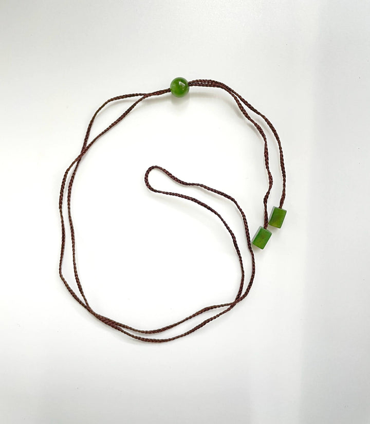 Brown braided cord necklace featuring a single round jade bead and two square jade beads