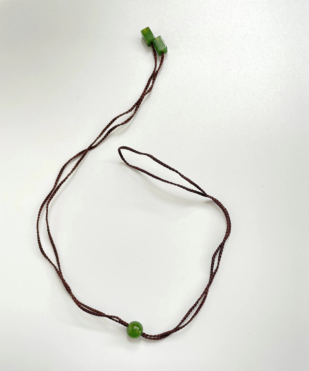 Brown braided cord necklace with jade beads two cube ends and a green round centerpiece