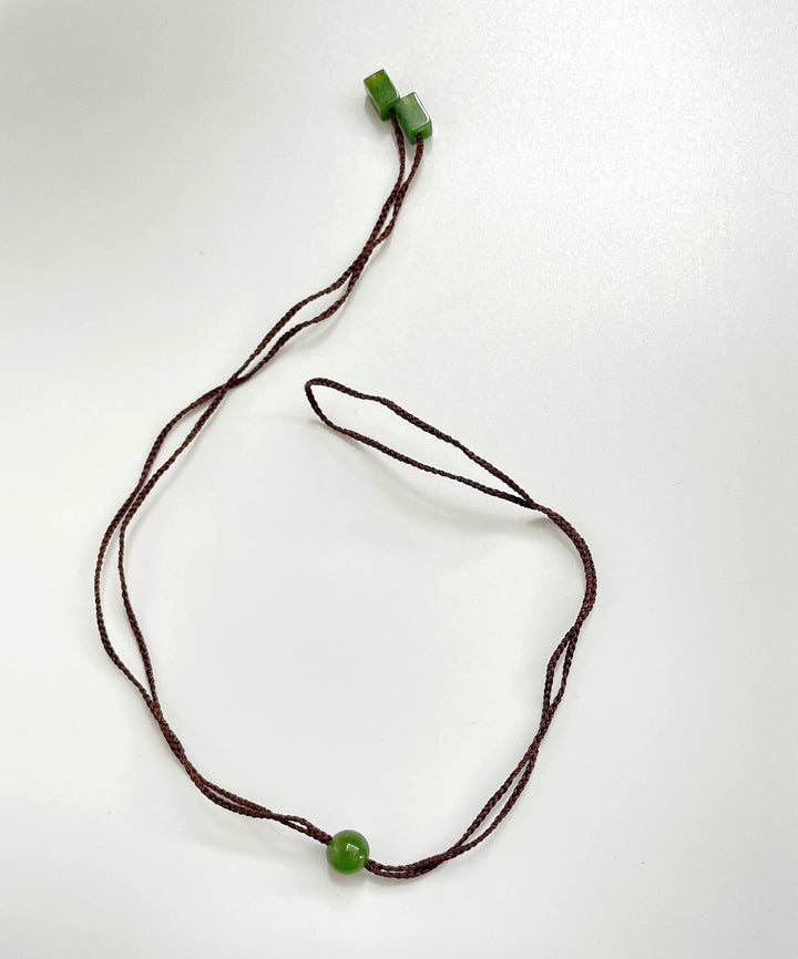 Brown braided cord necklace with jade beads two cube ends and a green round centerpiece