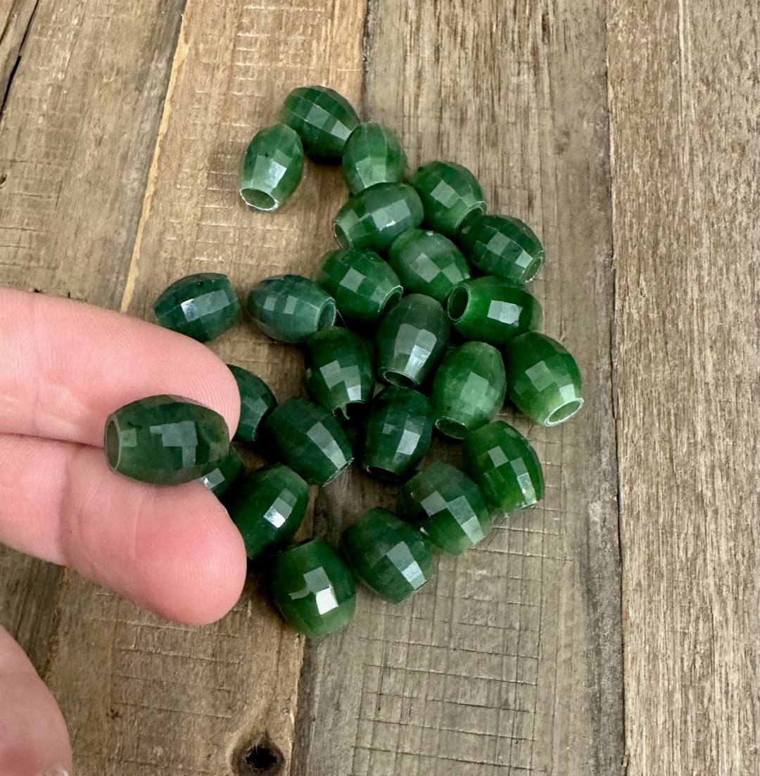 Cluster of faceted green jade beads with drilled holes scattered on a wooden surface.