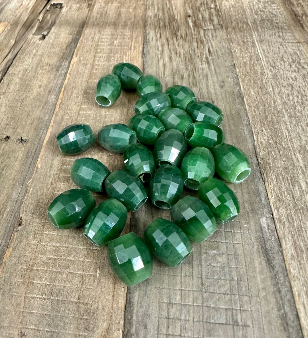 Cluster of faceted green jade beads with center holes scattered on a wooden board