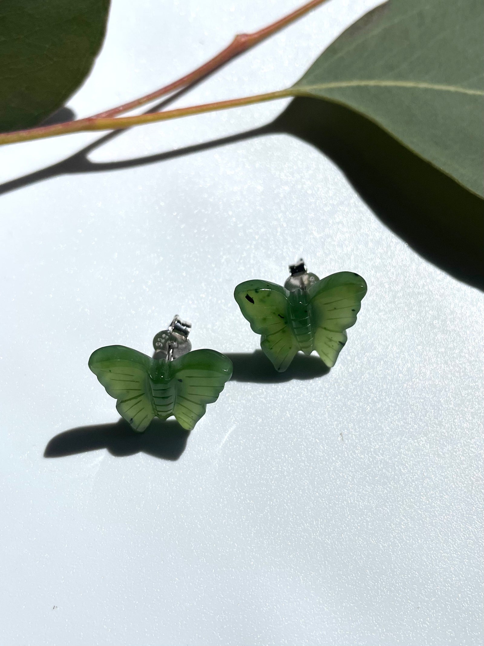 Green butterfly shaped earrings with silver posts on a white surface.