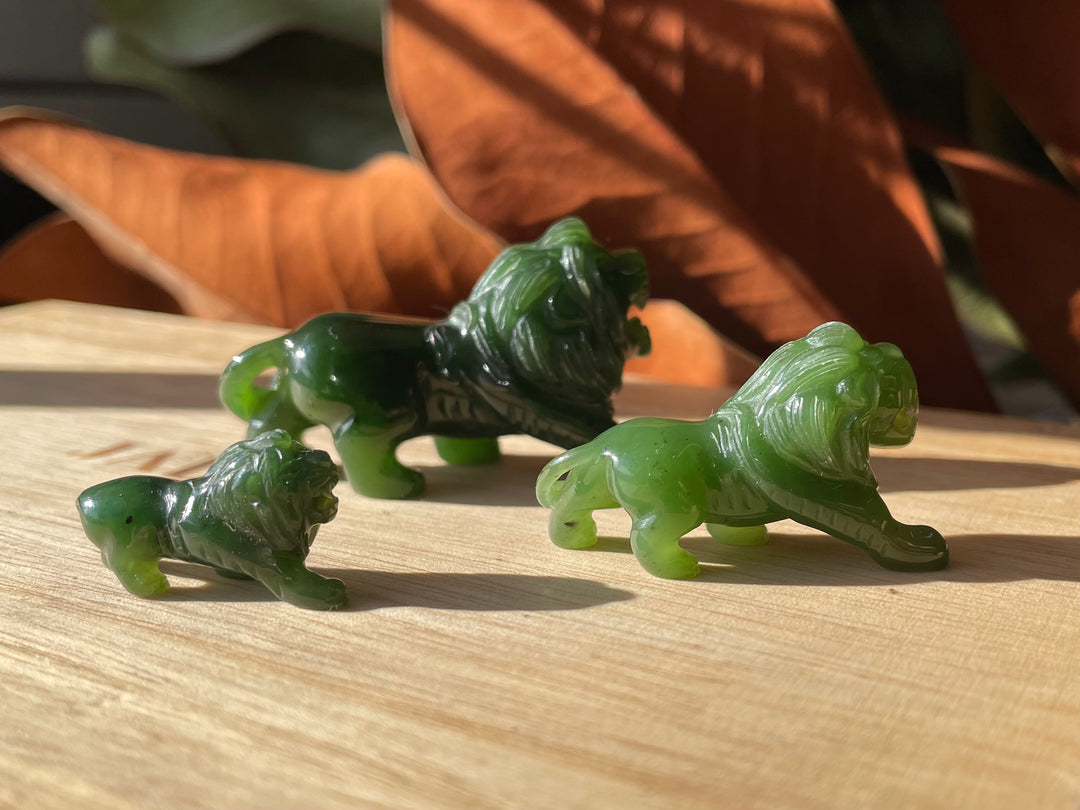 Group of jade green lion figurines on a wooden table with a larger rightmost lion and two smaller cubs