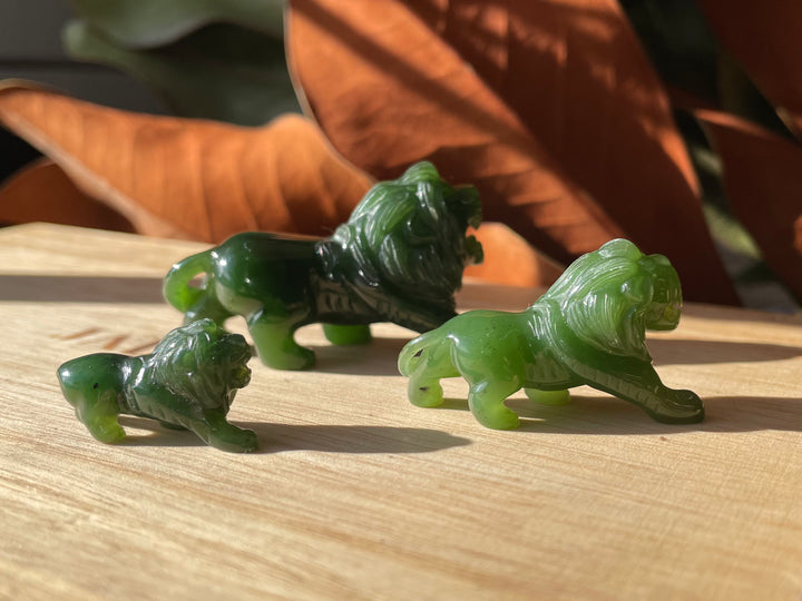 Group of jade green lion figurines on a wooden table with a larger rightmost lion and two smaller cubs