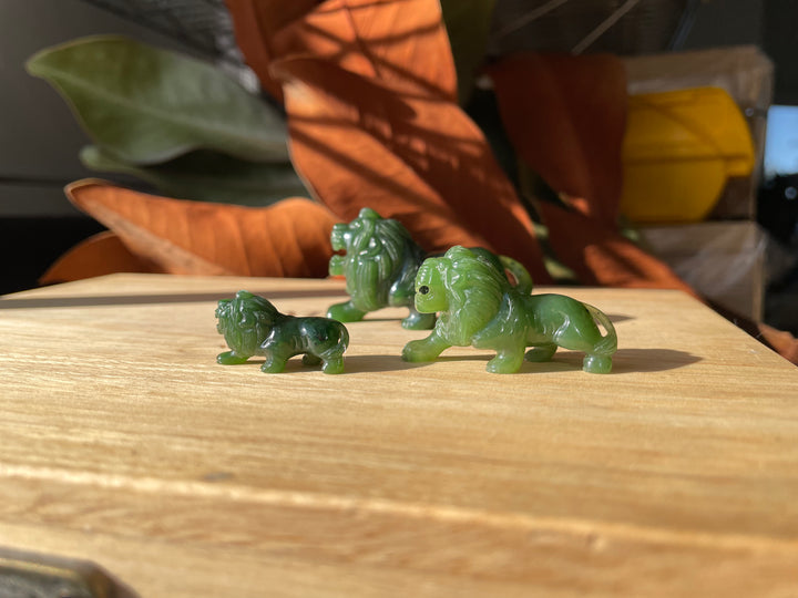 Three jade green lion statues on a wooden surface, including a large open mouthed adult and two smaller cubs