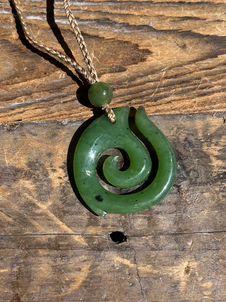Green jade spiral pendant on a braided cord laid on a rustic wooden surface.