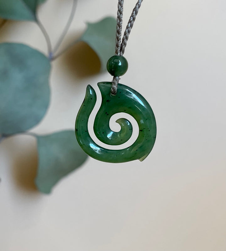 Close up of a green jade spiral pendant suspended from a braided cord with a small bead above.