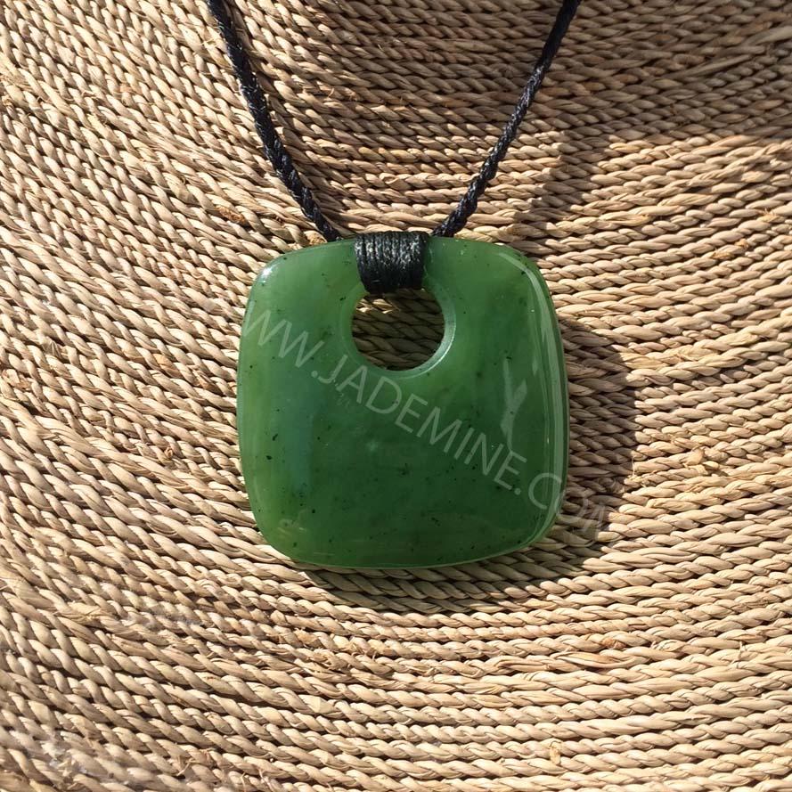 Close up of a green jade pendant with circular hole on a black cord against a woven straw background