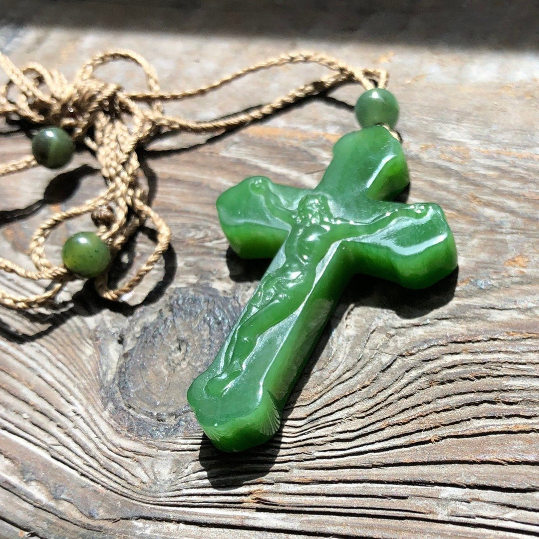 Green jade crucifix pendant with a carved Jesus on the cross, paired with a braided tan cord and round green beads