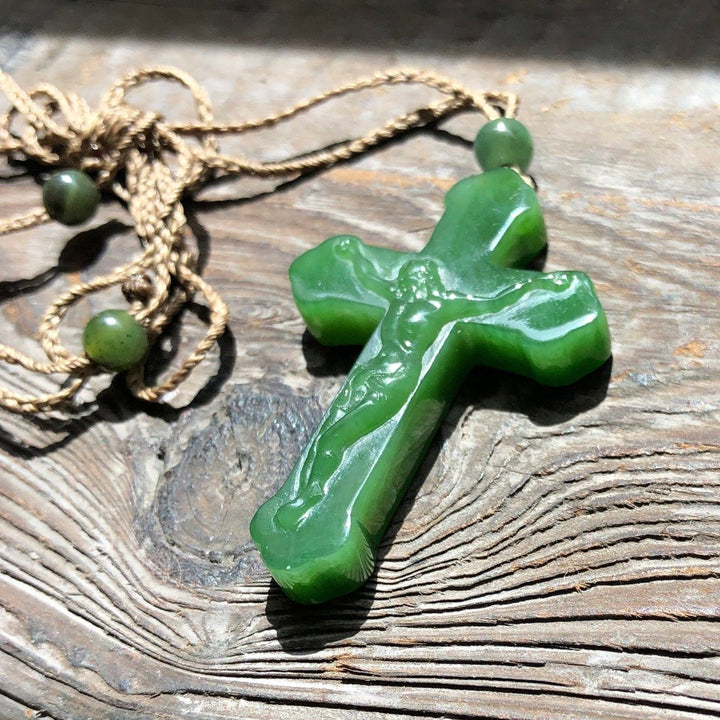 Green jade crucifix pendant with a carved Jesus on the cross, paired with a braided tan cord and round green beads