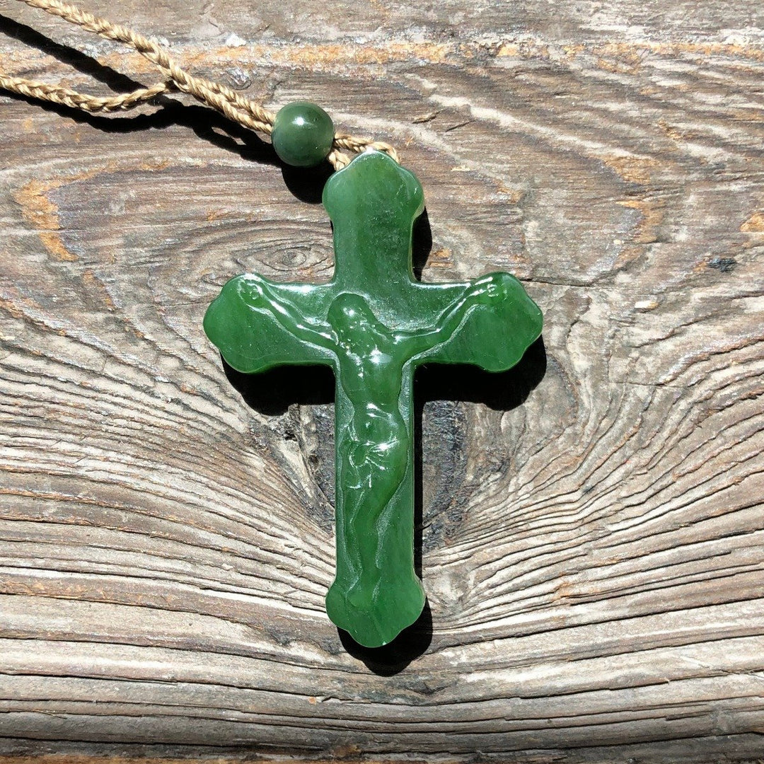 Jade crucifix pendant on a twisted jute cord against weathered wood.