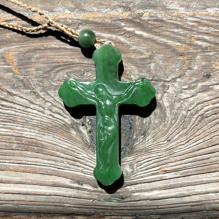 Jade crucifix pendant on a twisted jute cord against weathered wood.