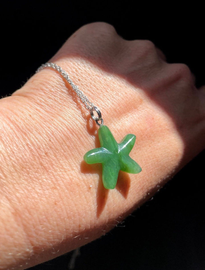 Green starfish charm pendant on a silver chain worn on the wrist