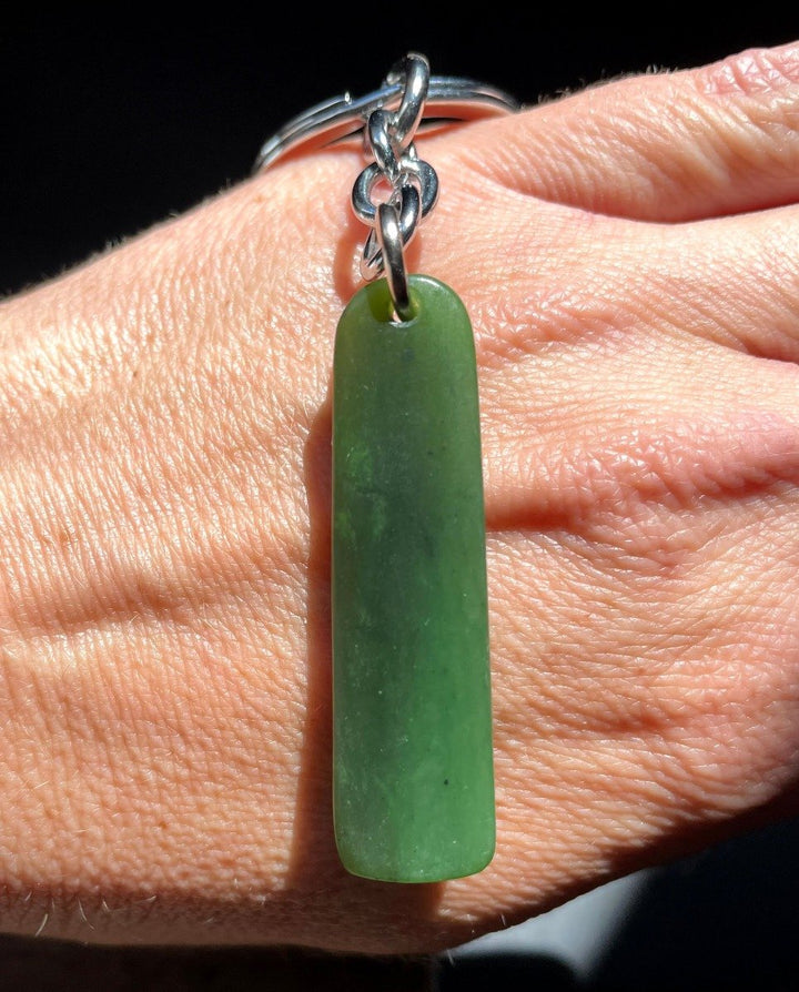Satin finish jade keychain pendant 1.7 inches long on a silver chain against a hand.