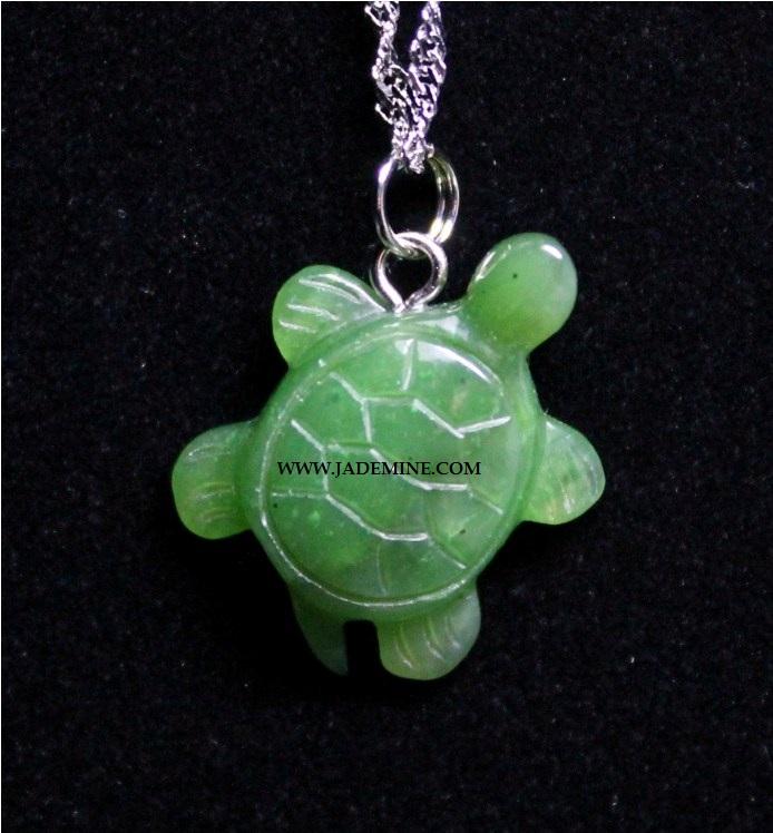 Close up of green turtle pendant on a silver chain against a black background