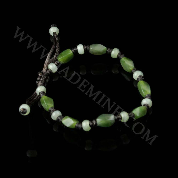 Green and pale green bead bracelet on dark cord with knotted spacers against a black background.
