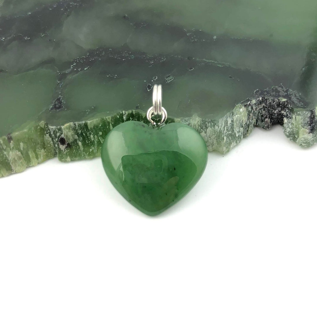 Green heart shaped pendant with a silver bail resting on a green stone surface