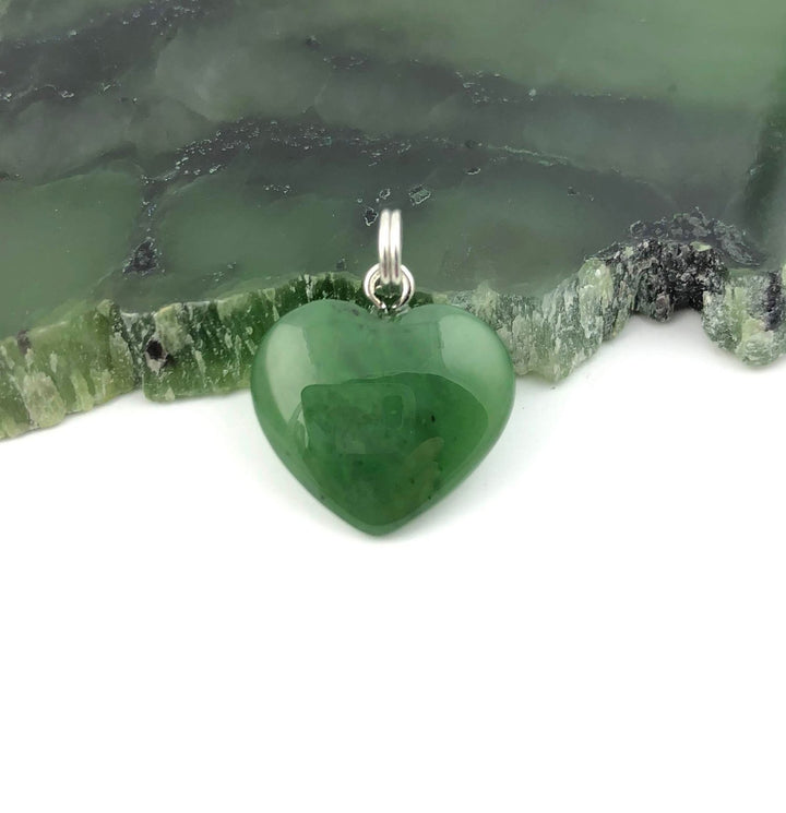 Green heart shaped pendant with a silver bail resting on a green stone surface