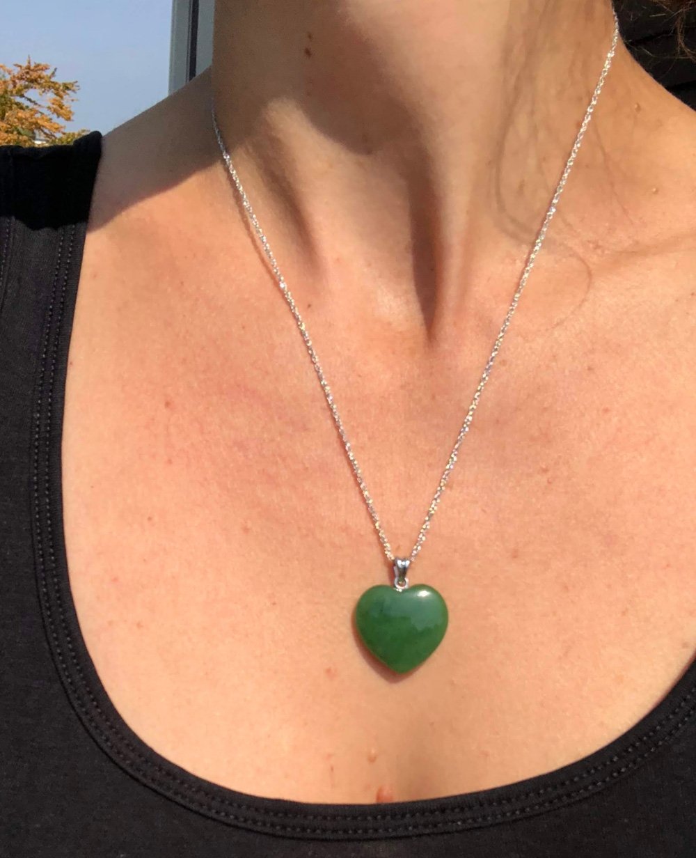 Heart shaped green jade pendant on a delicate silver chain worn around the neck.