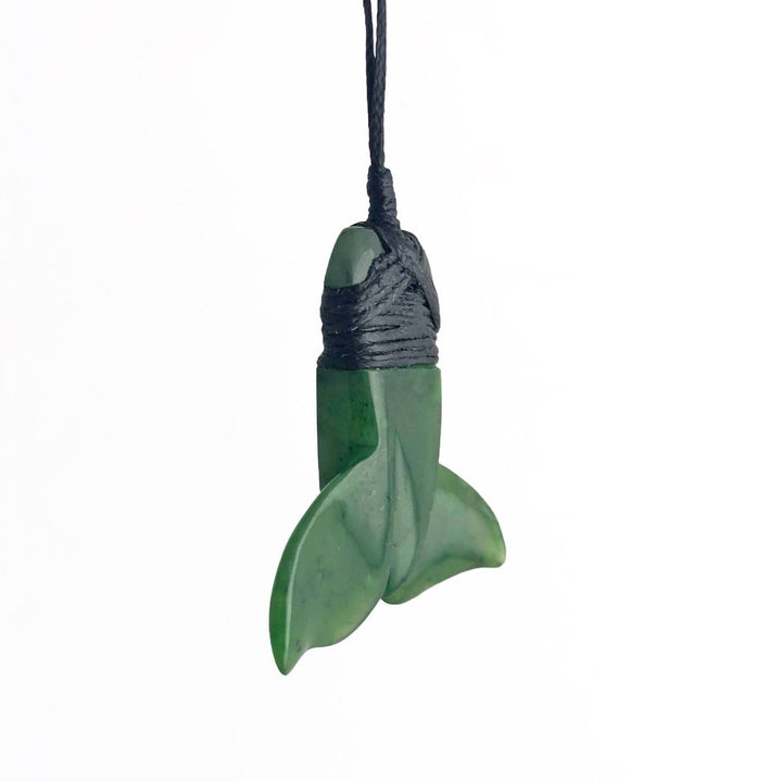 Close up of green jade whale tail pendant with cord wrapped around the top against a white background.