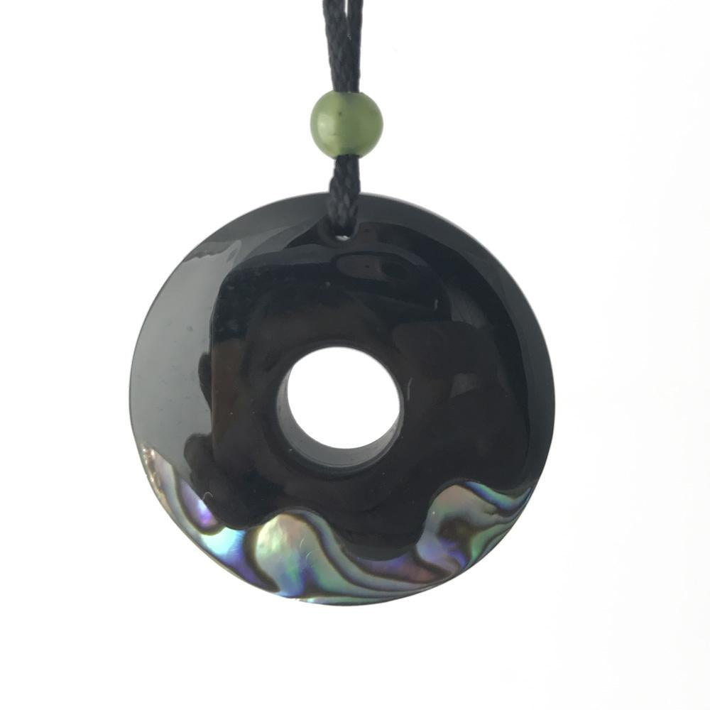 Donut shaped black pendant with a central hole on a cord, accented by a green bead above